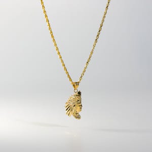 Puede incluir: Un collar de cadena de oro con un colgante que presenta un perfil detallado de un nativo americano con un tocado.