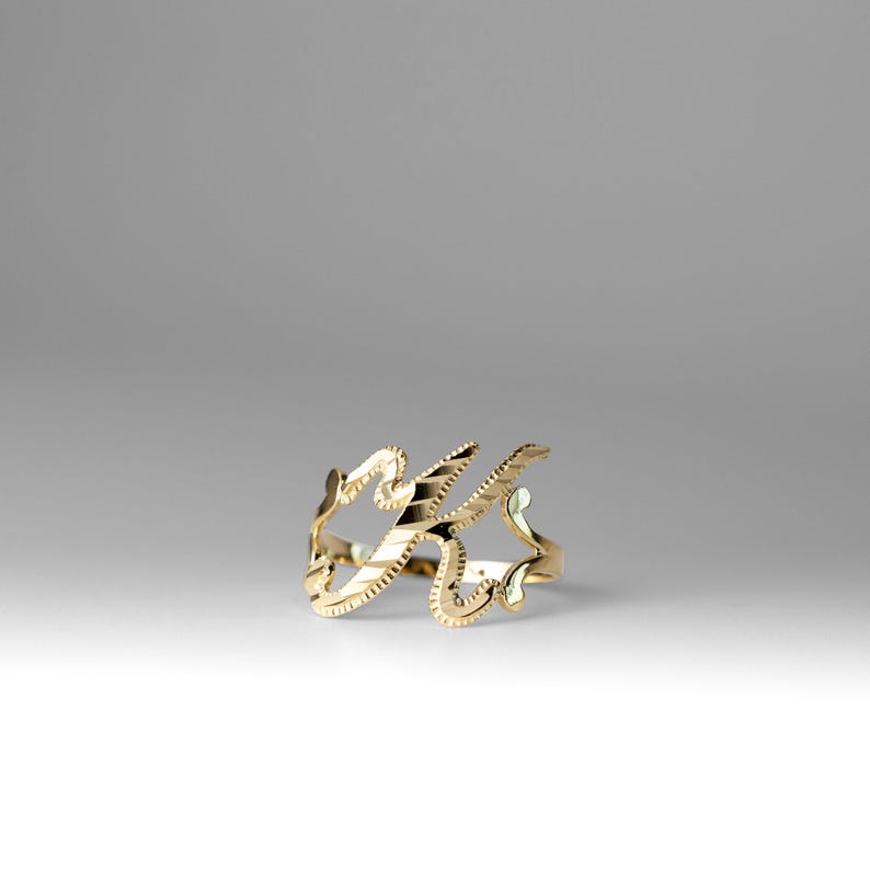 K&ouml;nnte beinhalten: Ein goldener Ring mit einem stilisierten K-Design.