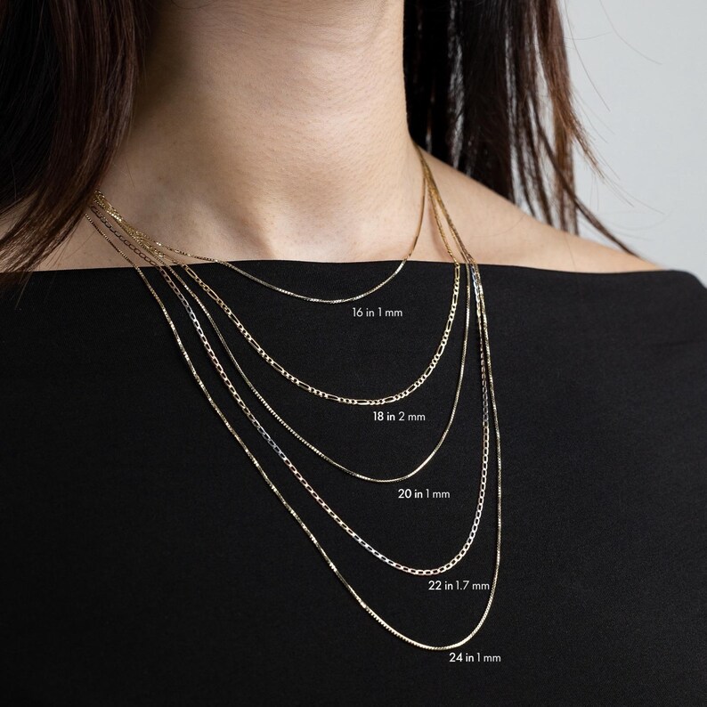 May include: Five gold chains of different lengths and widths, layered on a model's neck. The chains are labeled with their length and width in inches and millimeters: 16 in 1 mm, 18 in 2 mm, 20 in 1 mm, 22 in 1.7 mm, and 24 in 1 mm.