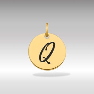 Pode incluir: Um pingente circular dourado com a letra cursiva preta "Q" no centro. O pingente tem uma pequena argola na parte superior para prender a uma corrente. O fundo é um gradiente cinza claro.