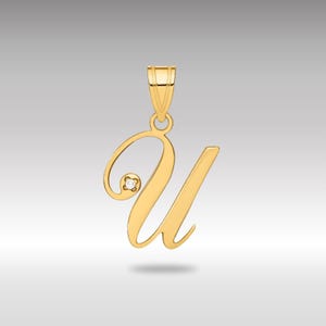 Può includere: Un ciondolo color oro a forma di lettera "U" in corsivo. Una piccola gemma rotonda e trasparente è incastonata nella curva della lettera. Il ciondolo ha un anello nella parte superiore per una catena.