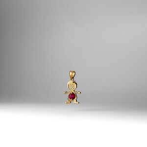 Puede incluir: Un colgante de oro en forma de niño con una piedra preciosa roja en el centro.