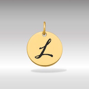 Puede incluir: Colgante circular dorado con la letra cursiva negra "L". El colgante tiene un pequeño lazo en la parte superior para una cadena. El fondo es un degradado de gris claro.