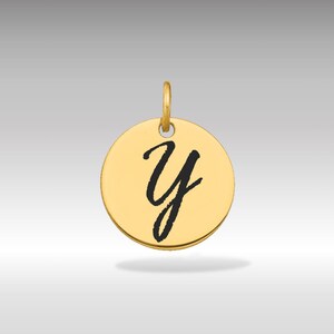 Puede incluir: Un colgante circular dorado con la letra cursiva "Y" negra en el centro. El colgante tiene un pequeño lazo en la parte superior para una cadena. El fondo es un degradado gris claro.
