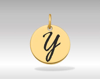 Puede incluir: Un colgante circular dorado con la letra cursiva "Y" negra en el centro. El colgante tiene un pequeño lazo en la parte superior para una cadena. El fondo es un degradado gris claro.