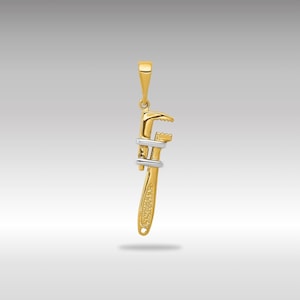 Könnte beinhalten: Ein verstellbarer Schraubenschlüssel-Anhänger aus Gold und Silber. Der Schraubenschlüssel ist mit einer strukturierten Oberfläche verziert und hat oben eine Öse zum Anbringen an einer Kette.