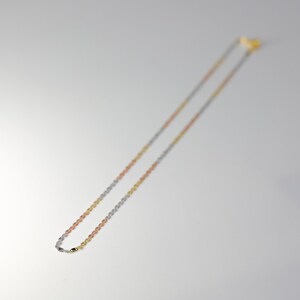 May include: A gold, silver, and rose gold chain necklace. The chain is made of small, linked ovals.