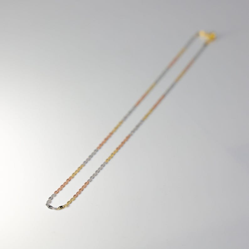 May include: A gold, silver, and rose gold chain necklace. The chain is made of small, linked ovals.