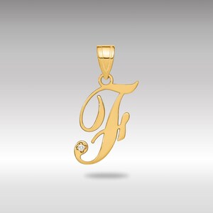 Può includere: Un ciondolo color oro a forma di lettera "F" in corsivo. Il ciondolo ha un piccolo accento di diamante e un anello per una catena. Il ciondolo è probabilmente in oro ed è progettato per essere indossato come gioiello.