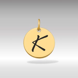 Pode incluir: Um pingente circular dourado com a letra "K" preta, em estilo manuscrito. O pingente tem uma pequena argola na parte superior para uma corrente. O fundo é um gradiente de cinza claro.