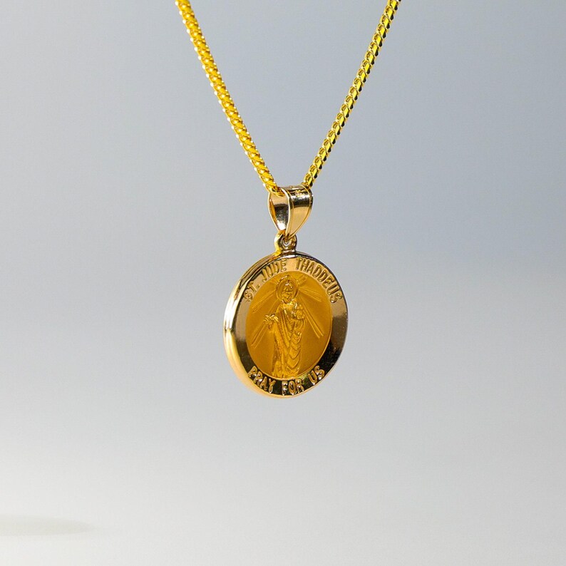 May include: A gold chain necklace with a round pendant featuring a depiction of Saint Jude Thaddeus. The pendant has the words "St. Jude Thaddeus" and "Pray for Us" inscribed around the image.