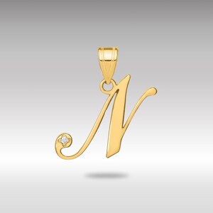 Könnte beinhalten: Ein goldfarbener Anhänger in Form des Buchstabens "N". Der Anhänger hat einen kleinen Diamantakzent und eine Schlaufe für eine Kette. Das Design ist elegant und für eine Halskette geeignet.