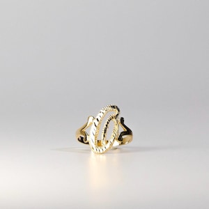 Puede incluir: Un anillo dorado con un diseño ovalado abierto. El anillo presenta una superficie texturizada y un patrón calado. El anillo está sobre un fondo blanco, resaltando sus intrincados detalles y artesanía.