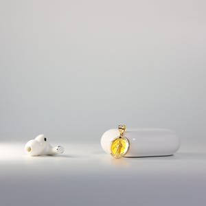 May include: A gold pendant with a yellow image of a religious figure on a white surface.