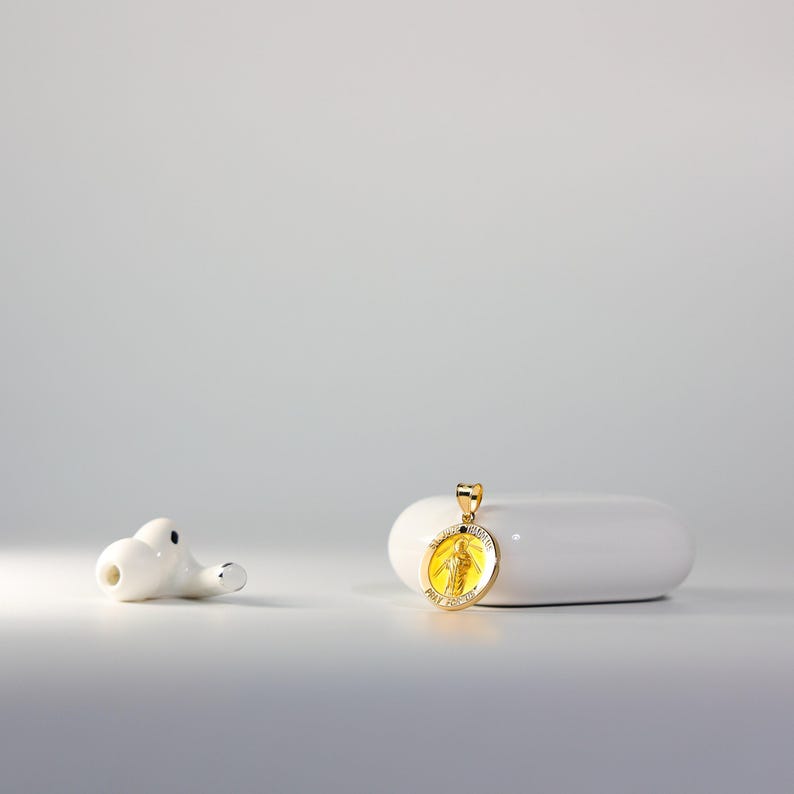 May include: A gold pendant with a yellow image of a religious figure on a white surface.
