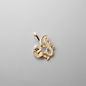May include: Gold-toned pendant featuring a cherub holding a stylized letter L.