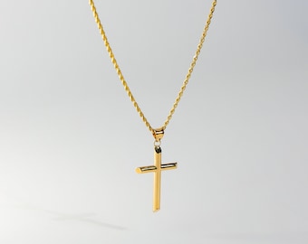 May include: A gold-colored cross pendant necklace. The cross is a simple, classic design with a polished finish. The chain is a delicate, twisted rope style. The necklace hangs against a plain, light background.