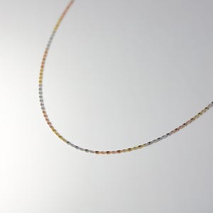 May include: A delicate chain necklace with three different colored metal links: silver, gold, and rose gold.