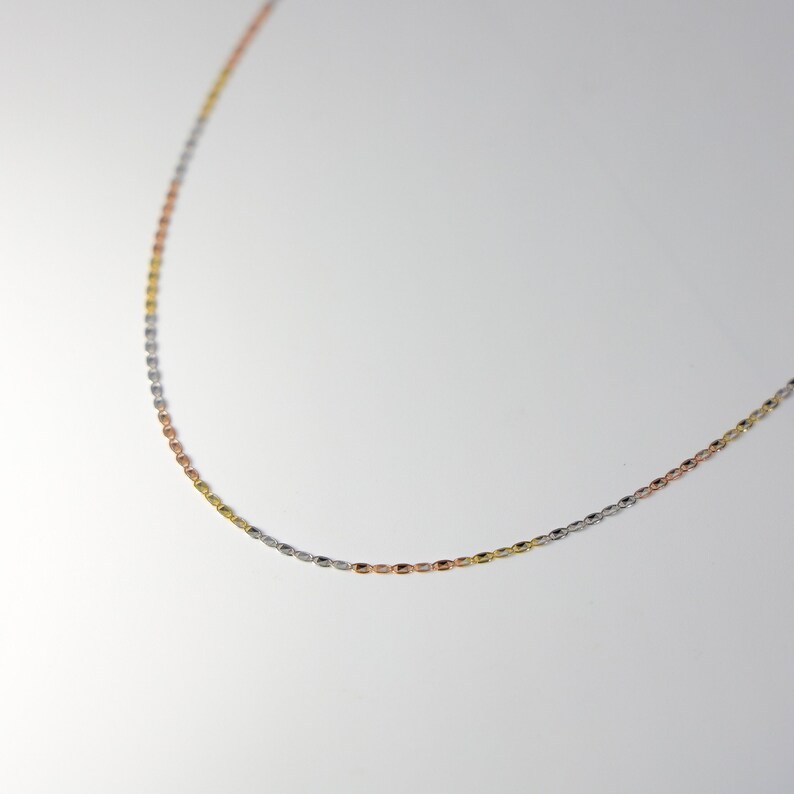 May include: A delicate chain necklace with three different colored metal links: silver, gold, and rose gold.