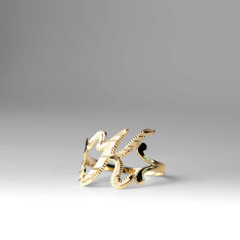 K&ouml;nnte beinhalten: Ein goldener Ring mit einem kursiv geschriebenen Buchstaben K.