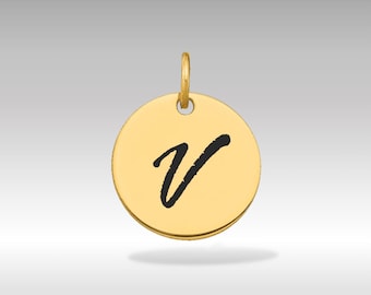 Puede incluir: Colgante circular dorado con la letra cursiva negra "V" en el centro. El colgante tiene un pequeño lazo en la parte superior para una cadena. El fondo es un degradado de gris claro a blanco.