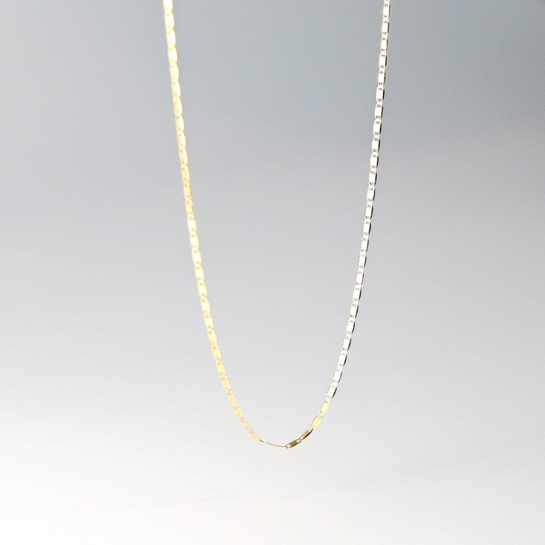 May include: A gold and silver chain necklace with a box chain design. The chain is made of metal and has a lobster clasp closure.