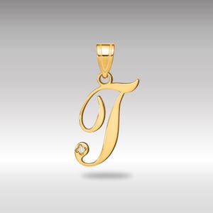 Può includere: Un ciondolo dorato a forma di lettera "T" in corsivo. Il ciondolo ha un piccolo diamante e un anello per una catena. Il ciondolo è probabilmente in oro ed è progettato per essere indossato come gioiello. Misura circa 2,5 cm di altezza.