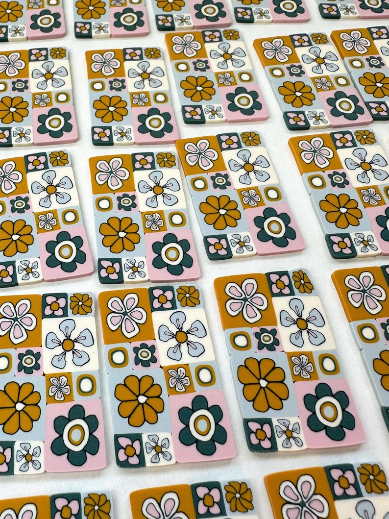 Op de afbeelding: Een verzameling handgemaakte keramische tegels met een retro bloemenpatroon. De tegels hebben een patchwork-ontwerp met roze, blauwe, witte, groene en gele bloemen op een witte achtergrond.