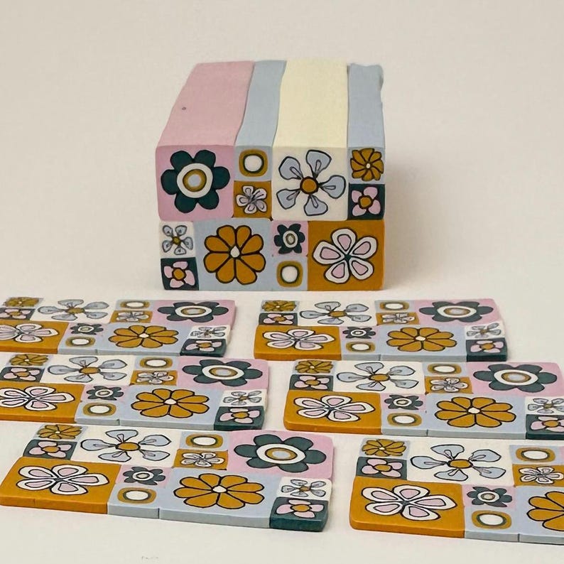 Op de afbeelding: Een set van zeven kleurrijke onderzetters met een geometrisch patroon van bloemen, cirkels en vierkanten in tinten roze, blauw, geel en groen.