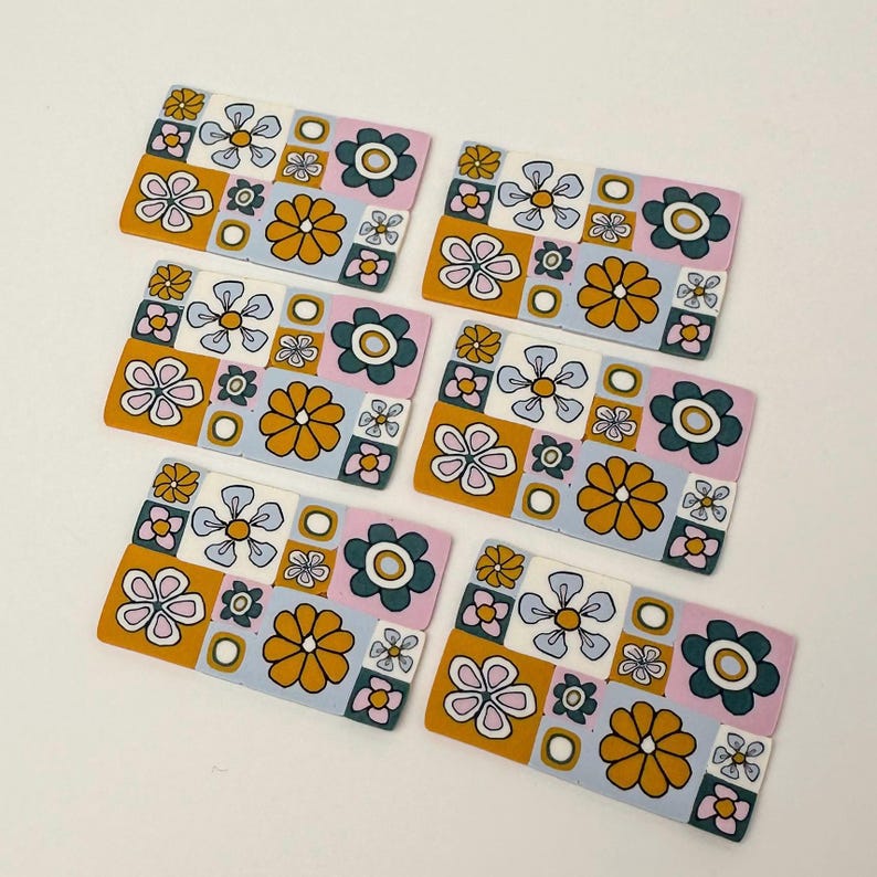 Op de afbeelding: Zes kleurrijke keramische tegels met een geometrisch patroon van bloemen en vierkanten in tinten blauw, roze, geel en groen.