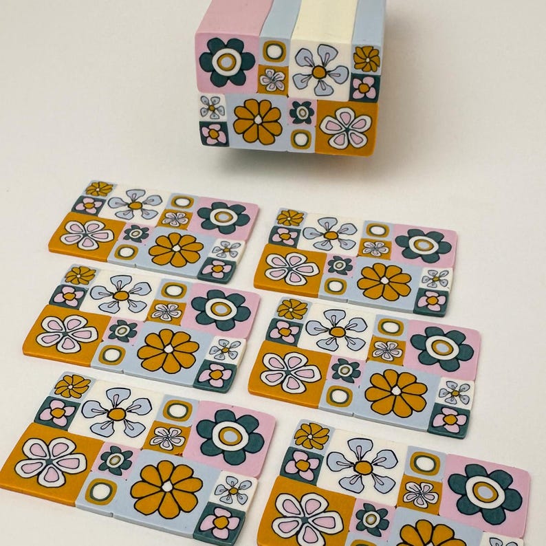 Op de afbeelding: Set van zeven kleurrijke onderzetters met een retro bloemenpatroon. De onderzetters zijn gemaakt van polymer clay en hebben verschillende kleuren, waaronder blauw, roze, geel en groen. De onderzetters zijn perfect om een vleugje vintage stijl aan elk huis toe te voegen.