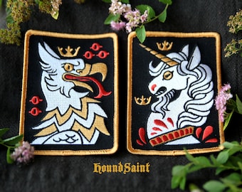May include: Two embroidered patches with black backgrounds and gold borders. One features a white griffin with a gold crown and red accents. The other shows a white unicorn with a gold crown and red accents. The text "HoundSaint" is at the bottom.