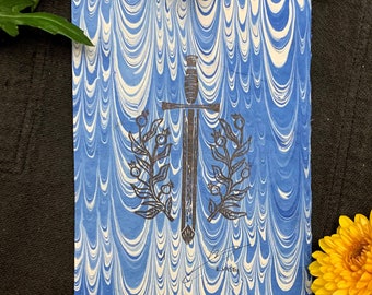 May include: A blue and white marbled notebook with a sword and laurel wreath illustration. The word "houndsaint" is printed at the bottom. Yellow flowers and green leaves are in the background.
