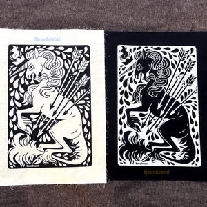 May include: Two rectangular fabric patches featuring a graphic illustration of a unicorn pierced by arrows. One patch is white with a black print, and the other is black with a white print. Both patches display the text "houndsaint" in a gothic font.