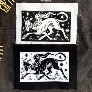 May include: Two fabric patches with a running greyhound design. One is black with a white illustration, the other white with a black illustration. The dog has a collar, stars, and floral elements. The text "houndsaint" is above the patches.