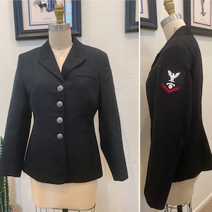 May include: A black blazer with silver buttons and a red and white eagle insignia on the left sleeve. The blazer has a notched collar and a single-breasted closure.
