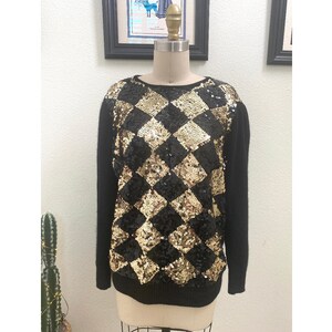 May include: A black sweater with a gold and black diamond pattern made of sequins.