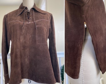 May include: A brown suede shirt with a lace-up collar and a side zipper. The shirt has a long sleeve and a fitted silhouette.