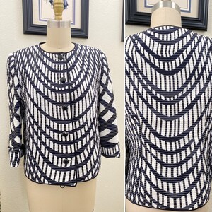 May include: A black and white geometric patterned jacket with a black trim and four black buttons. The jacket has a short sleeve and a slightly cropped length.