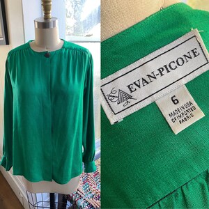 May include: A green long-sleeved button-up blouse with a round neckline. The blouse has a label that reads "Evan-Picone" and "Made in USA of Imported Fabric".