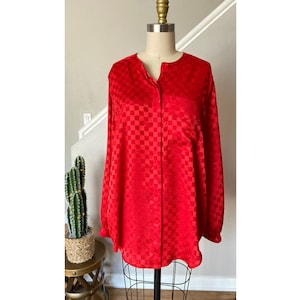 May include: A red long-sleeve blouse with a checkered pattern, displayed on a mannequin. The blouse has a mandarin collar, a single chest pocket, and button closures down the front. The fabric has a subtle sheen.