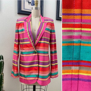 May include: A pink blazer with a colorful striped pattern. The stripes are red, orange, yellow, green, blue, purple, and white. The blazer has a single button closure.