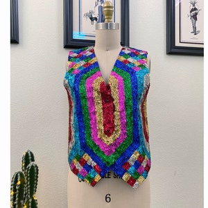 May include: A sleeveless vest with a rainbow pattern made of sequins. The vest has a V-neck and a button closure.