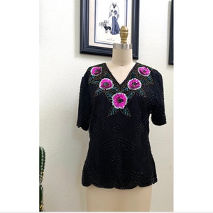 May include: A black sequined top with a V-neck and short sleeves. The neckline is adorned with a floral design featuring pink and green sequins.