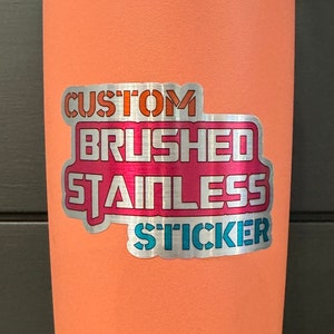 May include: A coral-coloured Yeti tumbler with a stainless steel lid and base. A sticker on the side reads "Custom Brushed Stainless Sticker".