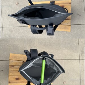 Puede incluir: Una mochila negra con una abertura con cremallera y un objeto verde en su interior. La mochila est&aacute; sentada sobre una superficie de madera. El texto "M12" es visible en la esquina inferior derecha de la imagen.