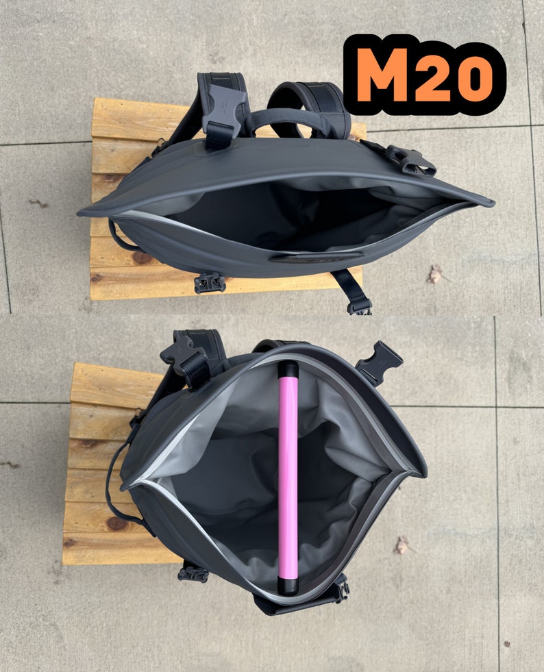 Puede incluir: Una mochila negra con una abertura con cremallera, que muestra el interior de la mochila. La mochila tiene un tubo rosa en el interior. La mochila tiene el texto "M20" en la parte superior.