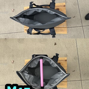 Puede incluir: Una mochila isot&eacute;rmica negra con una abertura con cremallera. La nevera est&aacute; abierta y hay un tubo rosa en su interior. La nevera est&aacute; sobre una superficie de madera. El texto "M15" est&aacute; en la esquina inferior izquierda de la imagen.