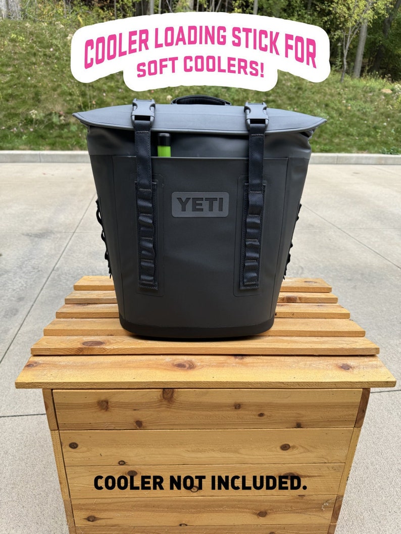 Puede incluir: Un enfriador suave Yeti negro con un palo de carga verde. El enfriador est&aacute; sentado en una caja de madera con el texto "COOLER NOT INCLUDED."  COOLER LOADING STICK FOR SOFT COOLERS! est&aacute; escrito en texto rosa sobre un fondo blanco.