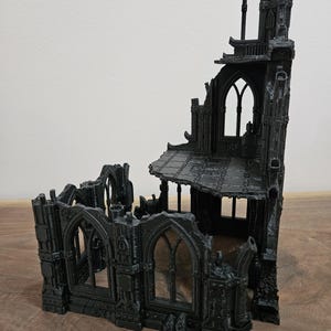 May include: A black miniature gothic building, possibly a ruined cathedral or castle, featuring arched windows and detailed architectural elements. The structure appears to be made of plastic or resin, with a textured surface.